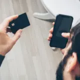 O persoană ține în mâna stângă un card bancar negru cu cip, iar în mâna dreaptă un telefon mobil cu ecranul stins sau negru